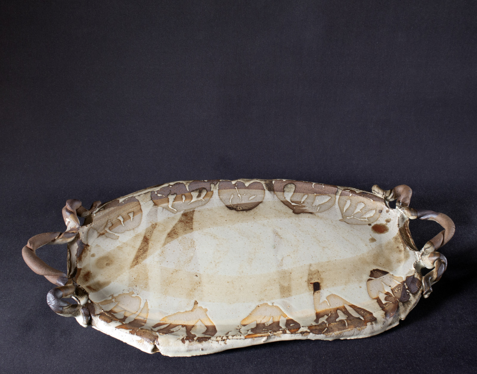 A red stoneware platter with wax-resist and ash glaze, and coiled handles