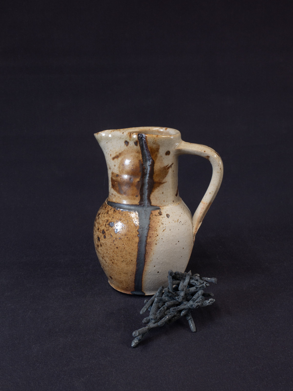 A wood-fired jug with a nail melted into its side and a cluster of melted nails