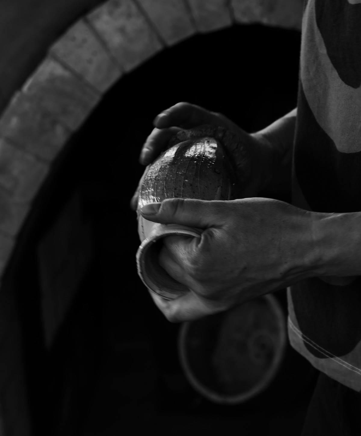 Rowena’s hands holding a wood fired bottle in front of the mouth of an anagama kiln