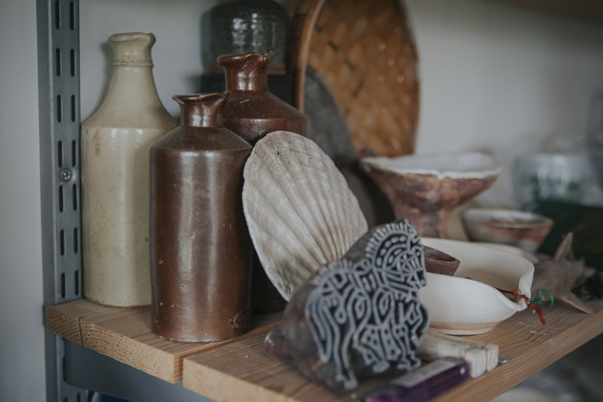 Old salt glazed bottles, scallop shell and wooden printing block on a studio shelf