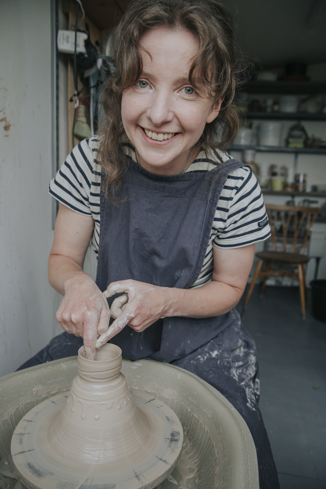 Rowena Hamilton smiling at the camera as she throws a tiny cup on the potters' wheel 'off the hump'